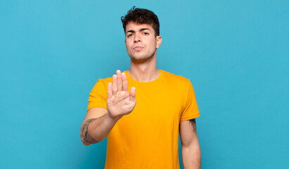 young man looking serious, stern, displeased and angry showing open palm making stop gesture