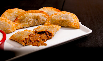 Deliciosos pasteis de carne, camarão, queijo com creme de queijo gorgonzola em recipiente branco em fundo escuro.