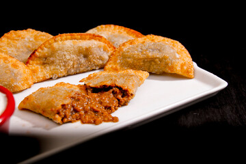Deliciosos pasteis de carne, camarão, queijo com creme de queijo gorgonzola em recipiente branco em fundo escuro.