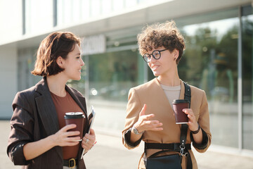 Two colleagues with drinks discussing working points in urban environment
