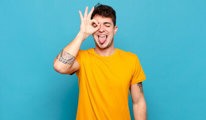 young man smiling happily with funny face, joking and looking through peephole, spying on secrets