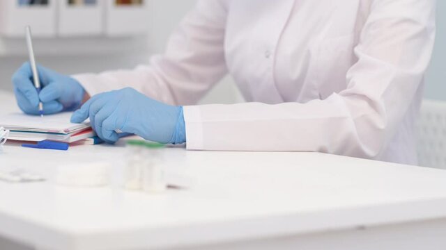 4k Unrecognizable woman doctor surgeon in white uniform is writing diagnosis and examination results. Hands in blue gloves close up. Healthcare and medicine