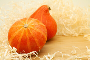 Two orange mini pumpkins on a wooden board. Wood shavings around the pumpkin. Place for text....