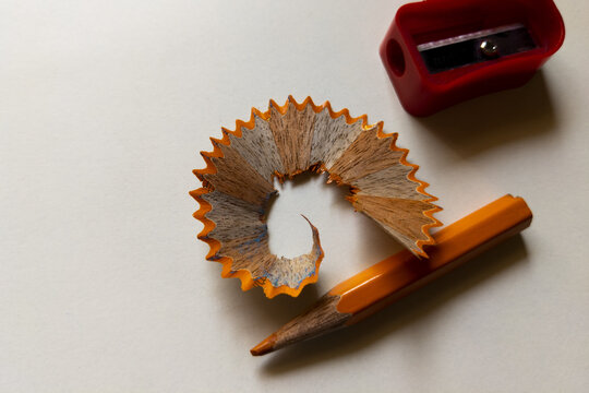 Top view closeup of an orange pencil with shavings and a red sharpener on a white background