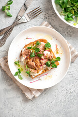 Tasty and healthy breakfast or lunch. Toast with tuna, ricotta cheese, and herbs in a white plate on a gray background top view. Mediterranean style breakfast.