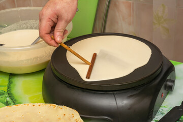Cooking breakfast in an electric pancake pan. Man's hand pours batter and spreads it over surface...