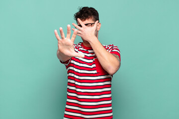 young man covering face with hand and putting other hand up front to stop camera, refusing photos...
