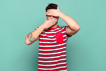 young man covering face with both hands saying no to the camera! refusing pictures or forbidding...