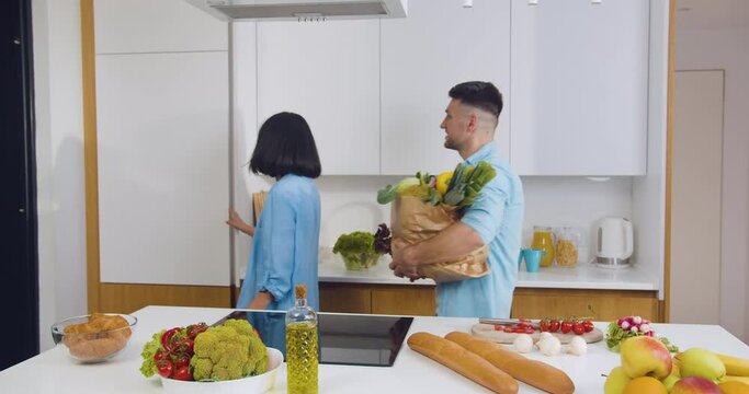Charming happy smiling couple in love came back from food market with big paper bag full of fresh groceries and put all products into fridge