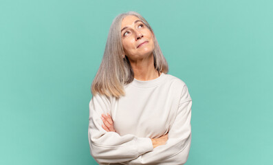 middle age woman feeling happy, proud and hopeful, wondering or thinking, looking up to copy space...