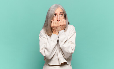 middle age woman looking worried, anxious, stressed and afraid, biting fingernails and looking to...