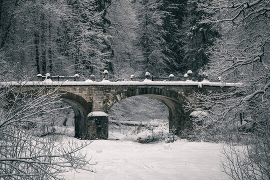 An old abandoned bridge in a winter park. Snowy winter day. Beautiful architecture. Mainly cloudy. A stone bridge.
