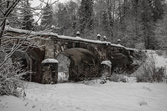 An old abandoned bridge in a winter park. Snowy winter day. Beautiful architecture. Mainly cloudy. A stone bridge.