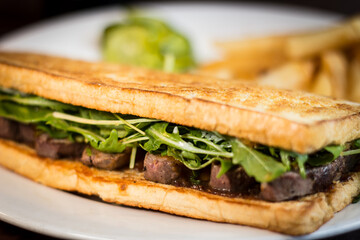 Steak sandwich with chips and pickles in a white dish