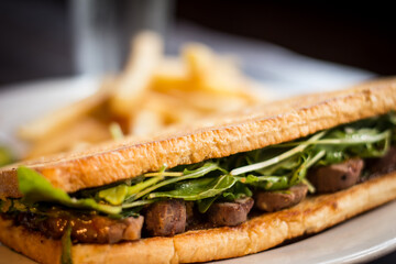 Steak sandwich with chips and pickles in a white dish