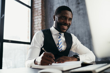 African American man sitting at a table in a tie smiling and writing in a notebook