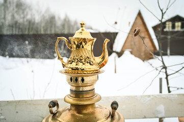 Obraz premium Beautiful golden teapot on heating samovar. Russian traditional tea machine. Private garden at winter.