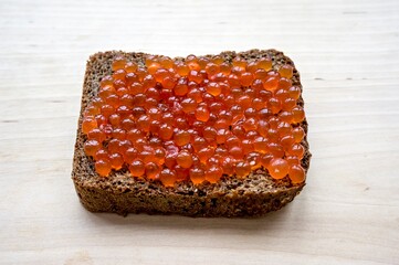 Sandwich with red caviar and rye bread on a wooden board