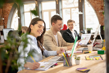 Laughting, smiling. Young caucasian colleagues working together in a office using modern devices and gadgets. Look busy, attented, cheerful, successful. Concept of business, office, finance.