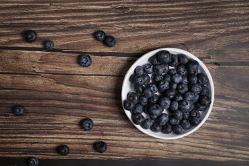 Top view of a white plate full of blueberries on a wooden table. Fruit vitamin.
