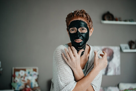 Young beautiful woman in a black cosmetic face mask. Spa treatment. Facial skin care at home. Mud face mask. Cosmetics for beautiful skin.
