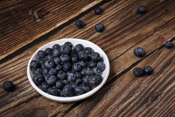 Top view of a white plate full of blueberries on a wooden table. Fruit vitamin.