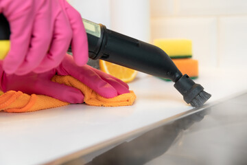 Women in rubber gloves cleaning black ceramic cooktop side with a hot steam cleaner.