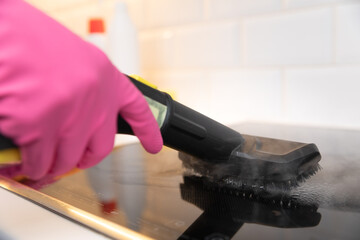 Housewife in rubber gloves cleaning black ceramic cooktop with a hot steam cleaner. Spring time cleaning.
