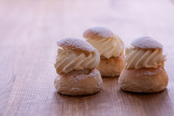 Three traditional Swedish pastry, the semla, on wooden table. This pastry is made of two-layer bun, stuffed with almond paste under a cover of thick layered whipped cream. Photo taken in Sweden.