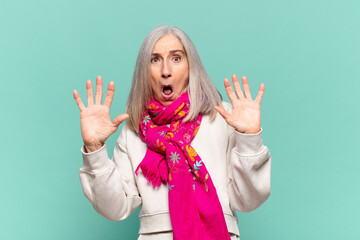 middle age woman feeling stupefied and scared, fearing something frightening, with hands open up...