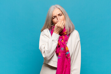 middle age woman feeling disgusted, holding nose to avoid smelling a foul and unpleasant stench