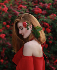 A beautiful red-haired girl in a red dress and red lips near gorgeous red roses.