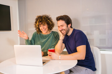 Lifestyle, a young Caucasian couple in pajamas having breakfast in the kitchen, making a family video call on the computer