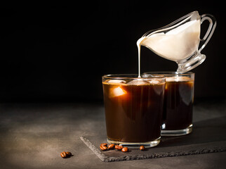 Ice coffee in a glass with cream poured over. gravy boat with milk levitates