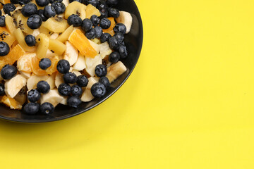 Fruit salad with blueberries, banana, orange, apple and kiwi on a black plate isolated on a yellow background. Vitamin cocktail. Summer taste.