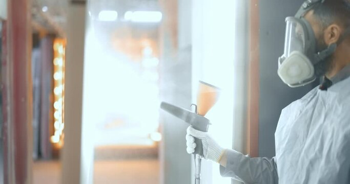 Painter in protective wear paints metal products with powder paint. Powder coating process at the manufacturing