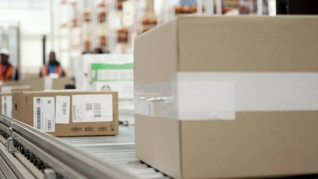 Packages and cardboard boxes traveling on an automated conveyor belt at large goods distribution warehouse.