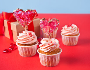 Valentines cupcake cream cheese frosting decorated with heart candy lollipop and gift box on the background.