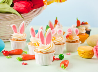 Easter funny bunny cupcakes. Easter celebration festive table. Basket of flowers tulips on the background.