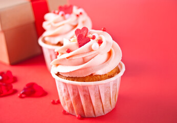 Valentines cupcakes cream cheese frosting decorated with heart candy and gift box on red background.