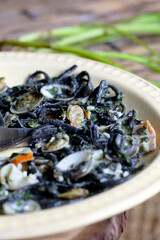 espaguete com tinta de choco, cozido com amêijoas e palitos de caranguejo estão em um prato. 