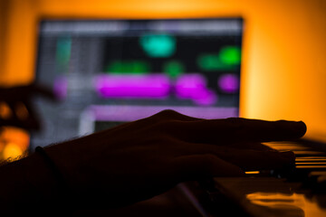 hand playing electric keyboard with blurred computer in the background