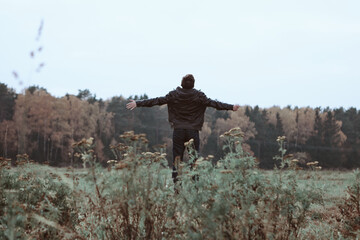 Naklejka na ściany i meble Man with arms outstretched to forest in a wild field. Freedom concept. Back view.