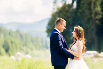 Happy young couple in a green field on their wedding day. Smiling newlyweds are walking in nature, holding hands. Family life.