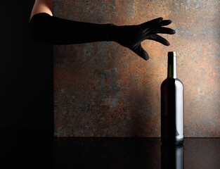 Woman hand in  glove reaches for a bottle of red wine.