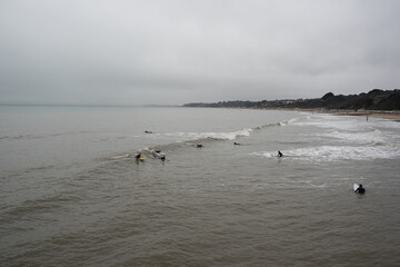 Bournemouth surfers in winter in sea with clouds overhead 