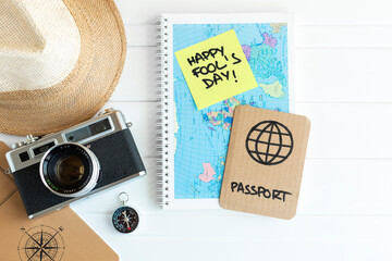 Desk with travel items such as camera, compass, hat and map next to a cardboard passport as a joke for Fool's Day celebration. Space for text. © Alfredo López