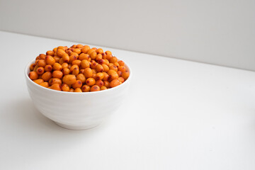 Deep white plate with sea buckthorn berries. Side view. On a two-tone background.