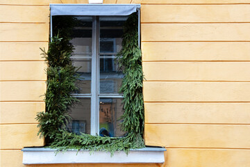 The window in the building is yellow, it is decorated with fir branches for Christmas