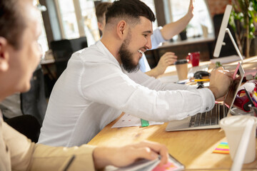 Creative workspace. Young caucasian colleagues working, laughting together in a office using modern devices and gadgets. Look busy, attented, cheerful, successful. Concept of business, office, finance